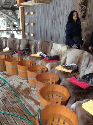 Auf der Huskyfarm wurden auf einer gedeckten Veranda mehrere Holzzuber mit warmem und duftendem Wasser im Halbkreis bereitgestellt. Die Stühle sind mit Fell ausgelegt.