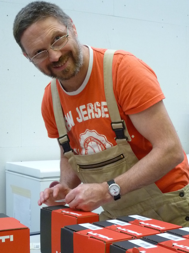 Ein Mann in orangem T-Shirt klebt Etiketten auf Pakete.